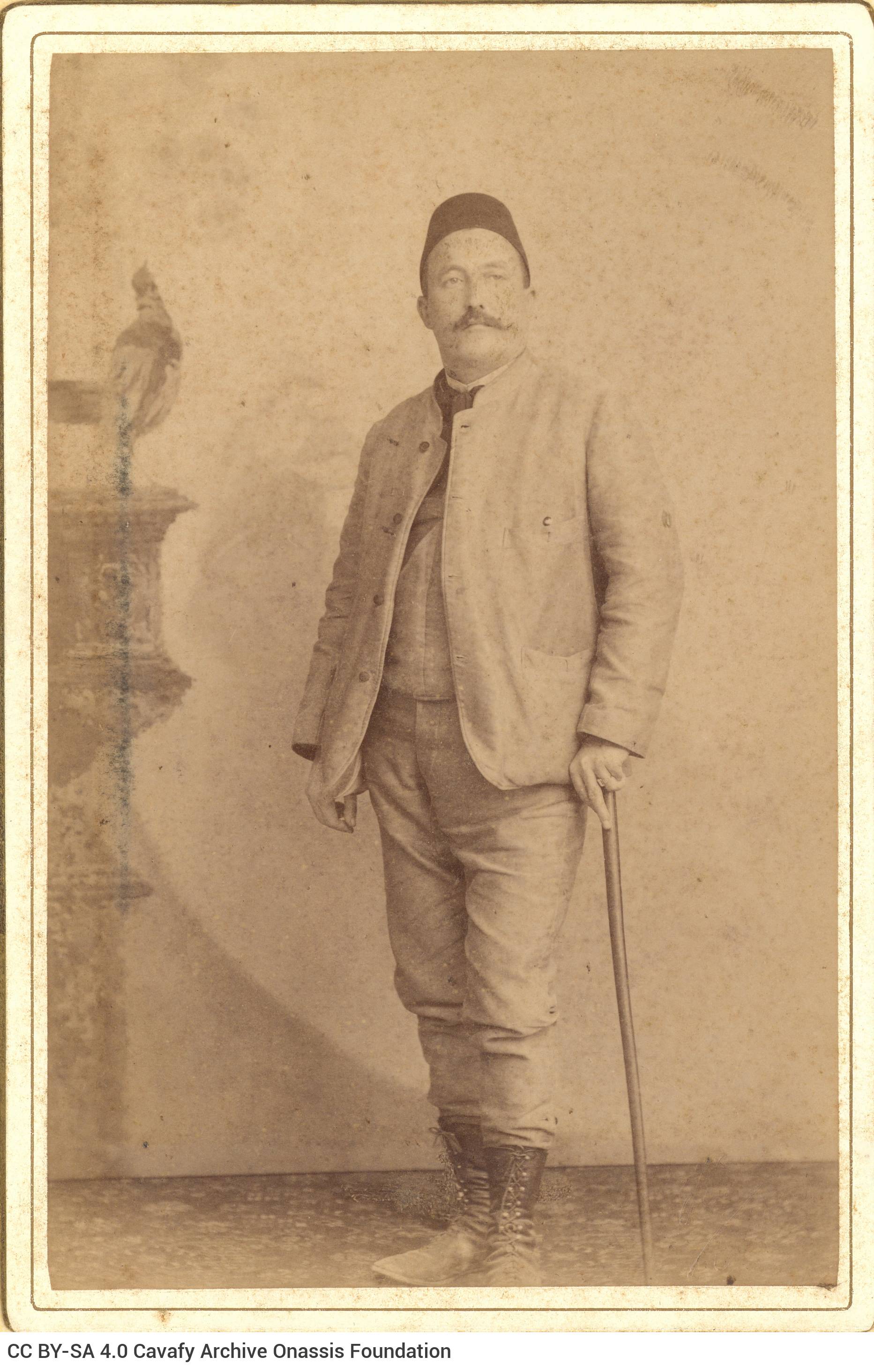 Undated photographic portrait of a man in a fez and with a cane in his left hand.