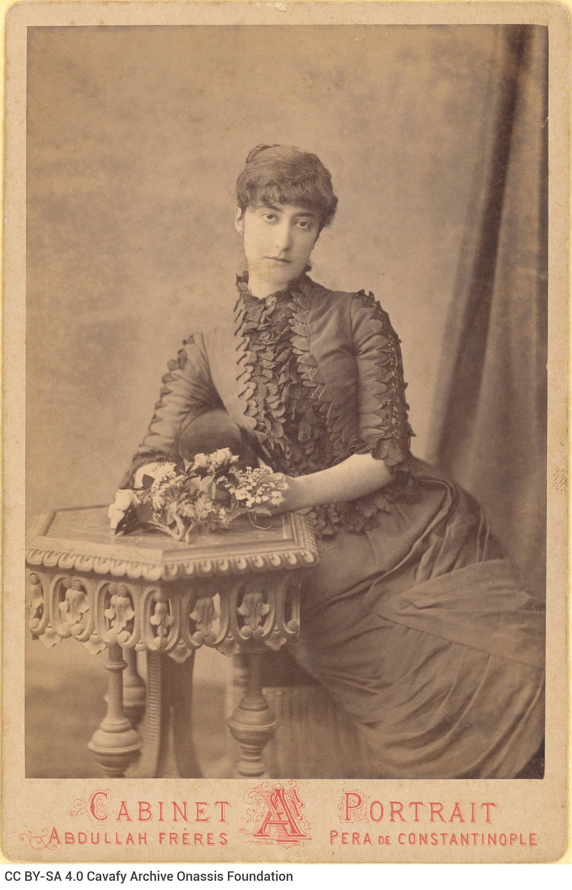 Photographic portrait of a seated woman with her hands on a table, holding flowers, from the Abdullah Frères photo shop of I
