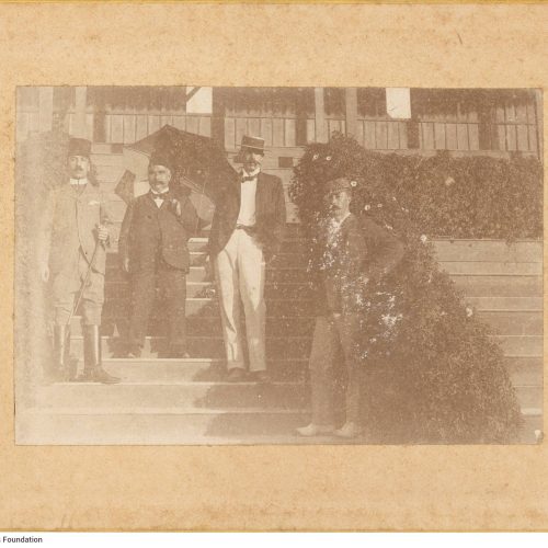 Photograph of four men on the stairs of a building. They are all wearing suits. The first from the left is wearing boots and 