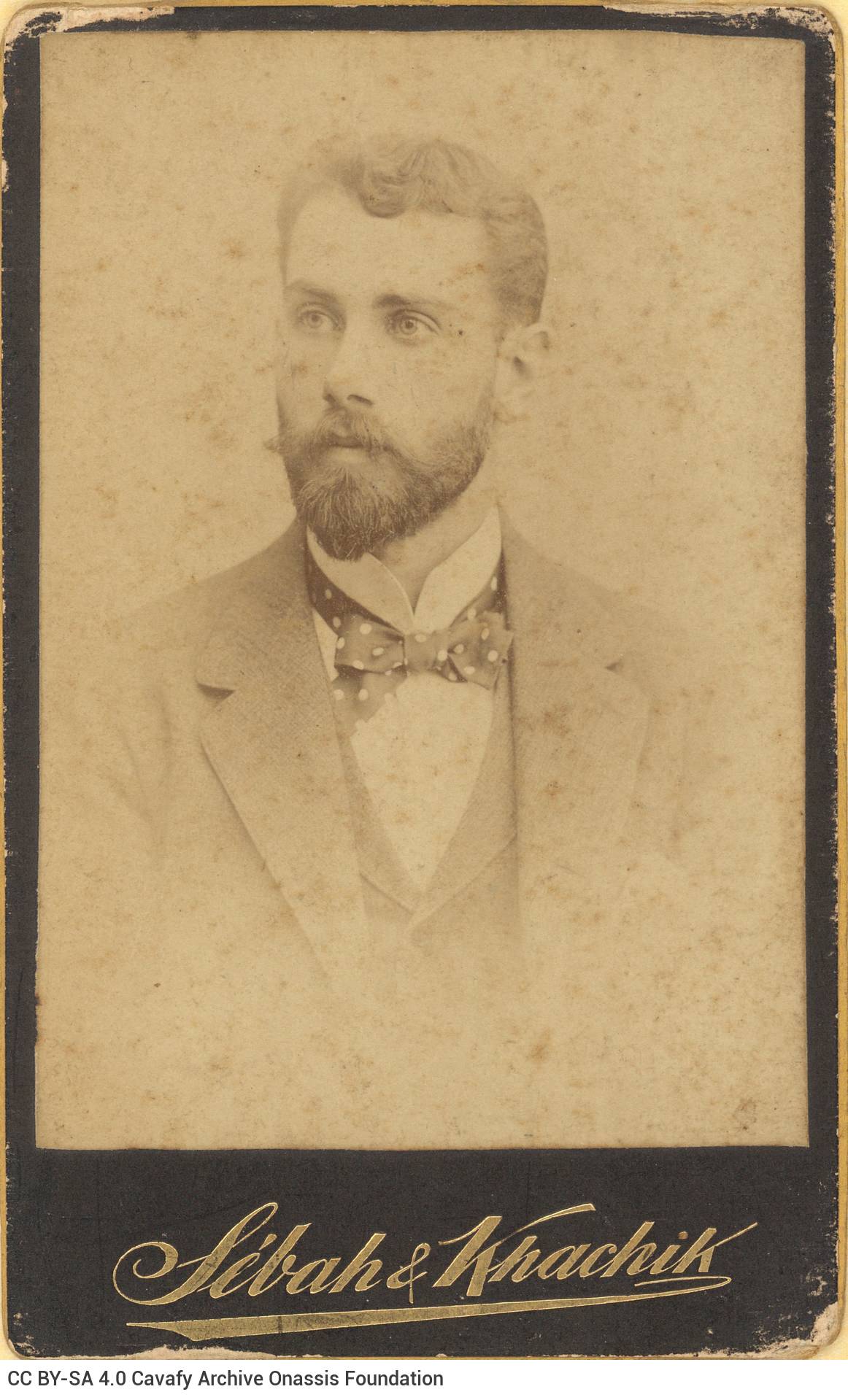 Photographic portrait of a young man in a suit, wearing a bow tie. The logo of the photo shop in the lower part of the recto 