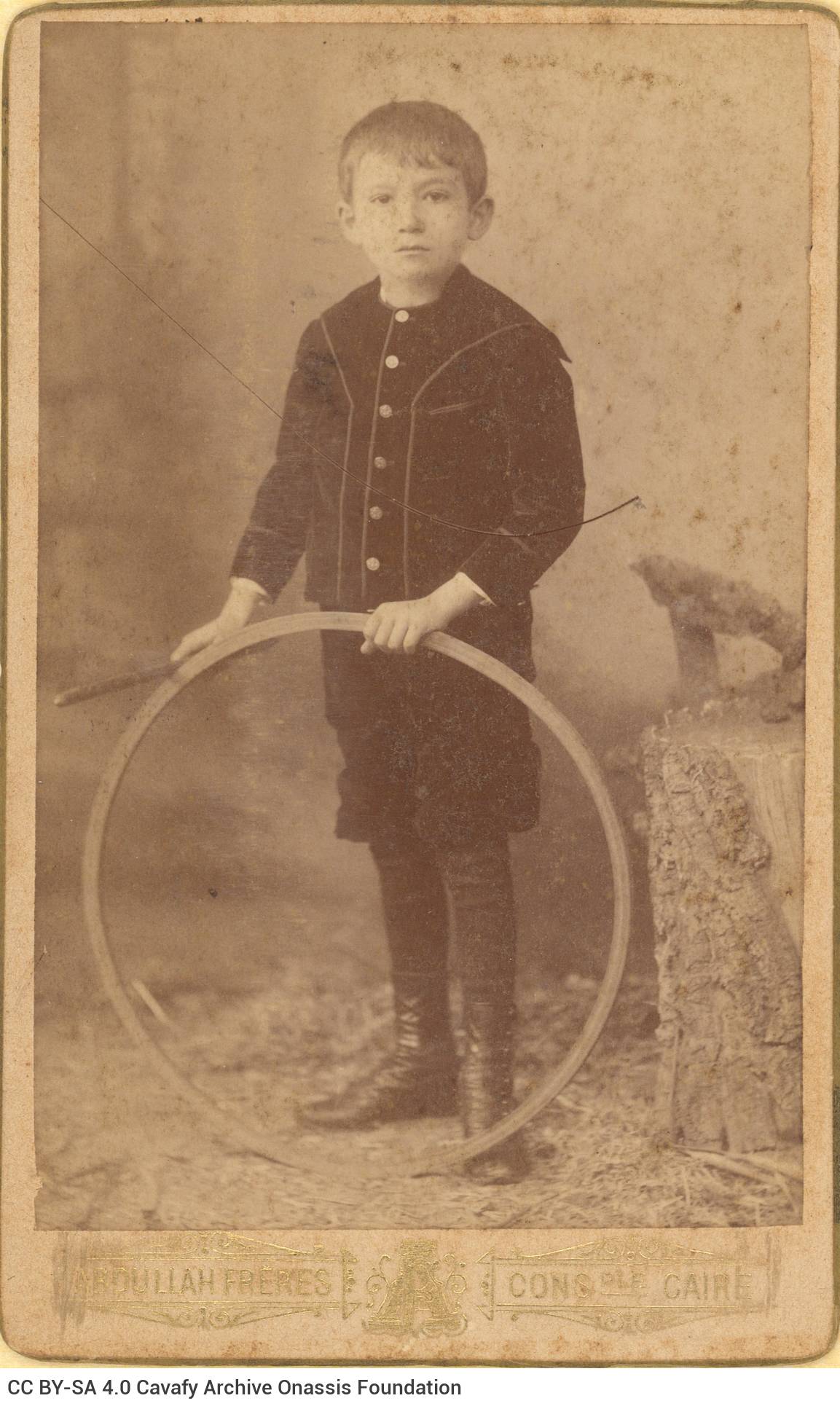 Photograph of a boy in dark clothes. It is holding a hoop and a stick. The logo of the photo shop in the lower part of the re