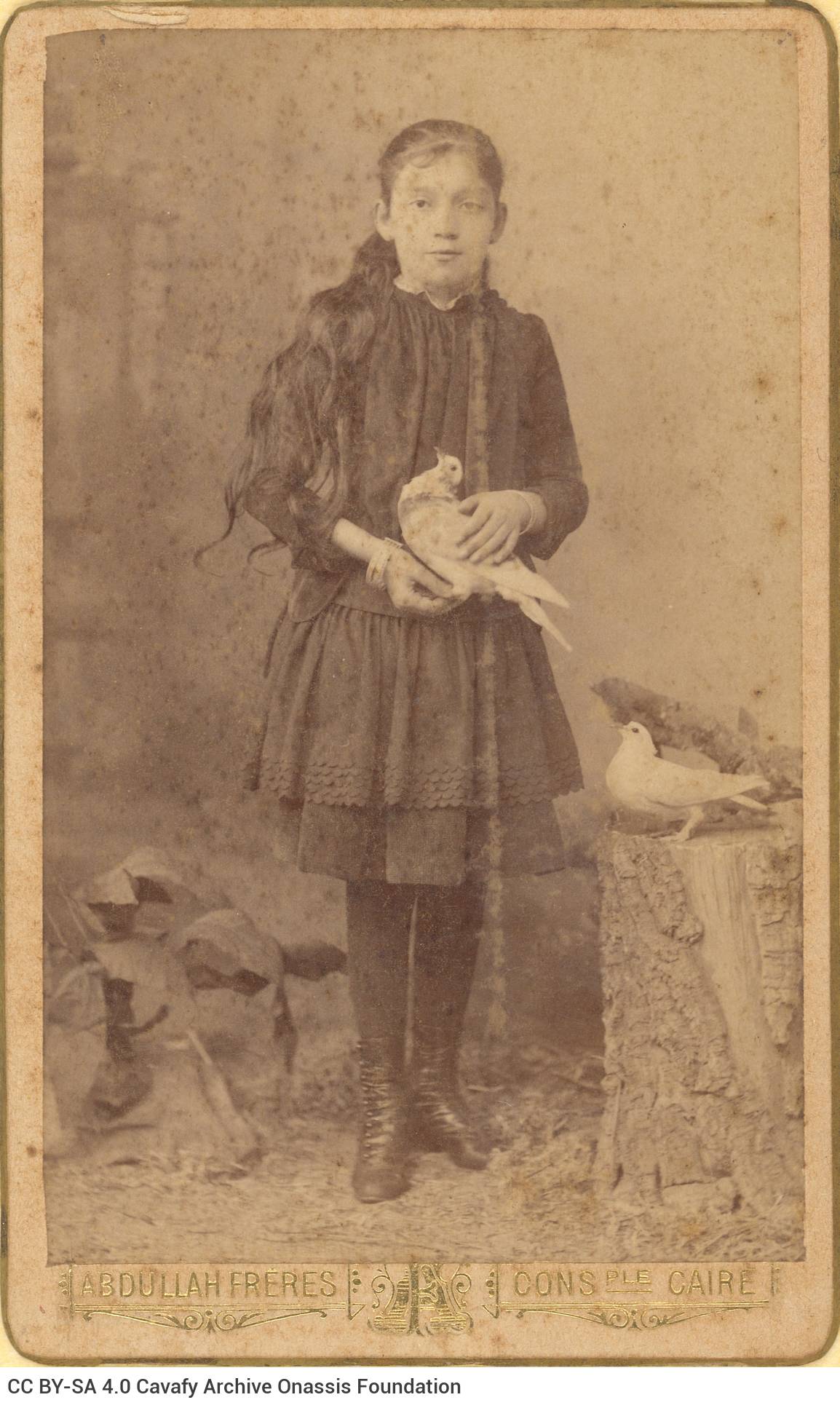 Photograph of a girl in dark clothes, holding a bird. The logo of the photo shop in the lower part of the recto as well as on