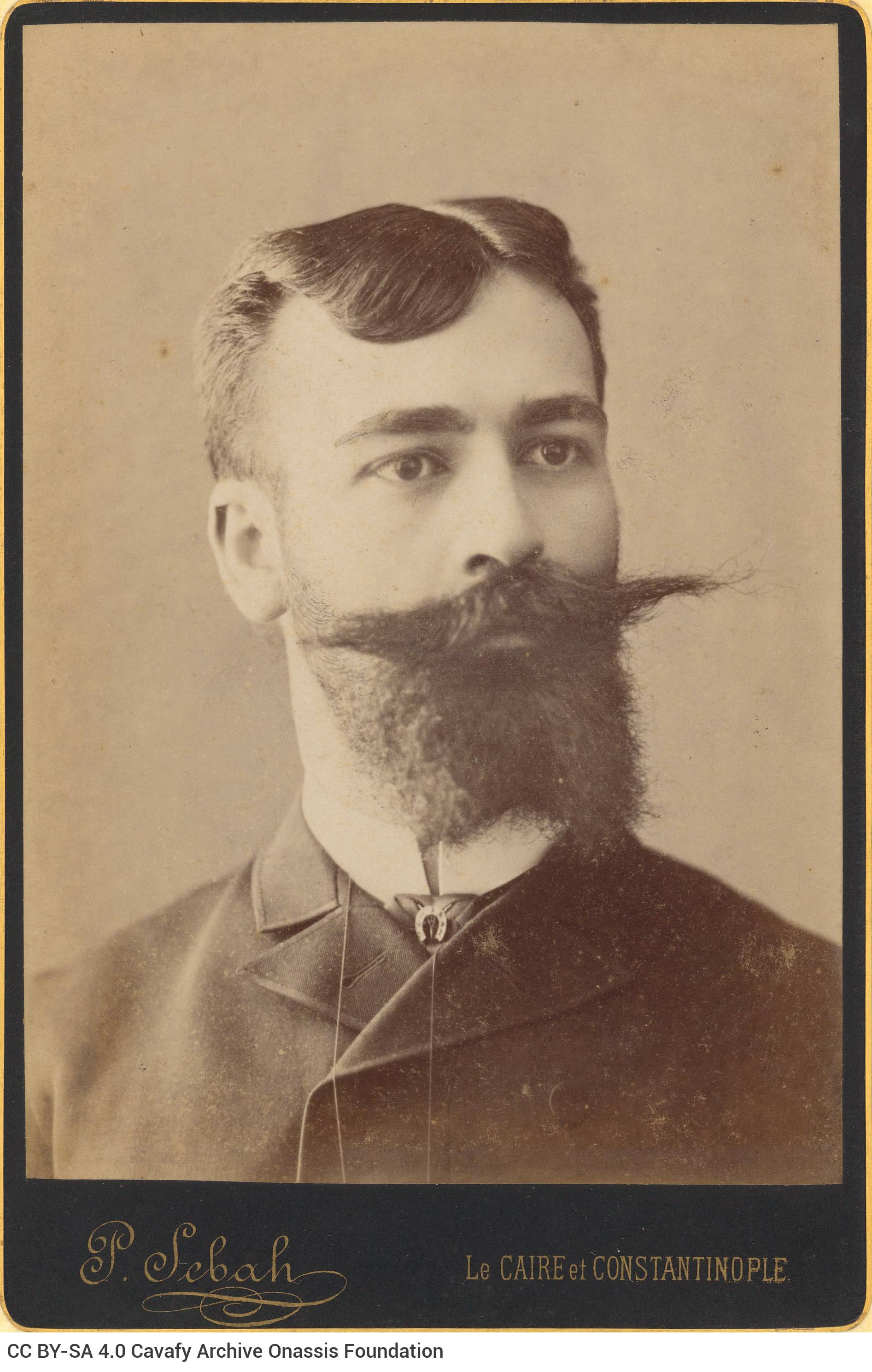 Photographic portrait of a young man with a large moustache and a beard. The photo shop's logo in the lower part of the recto