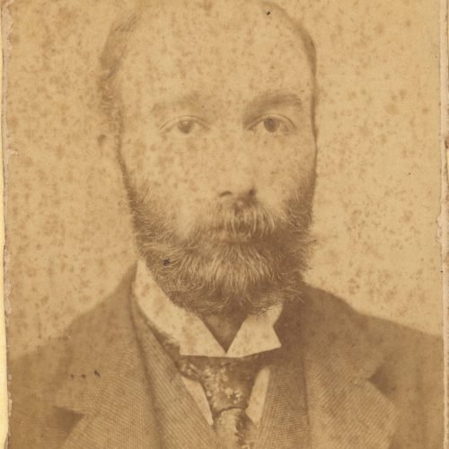 Photographic portrait of a man in a moustache and a beard, wearing a suit and necktie. In lower part of the recto, the printe