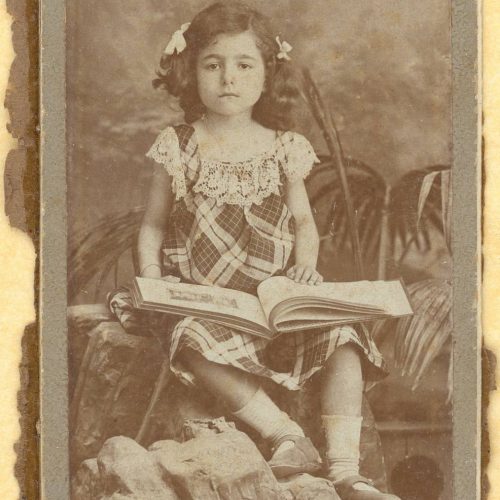 Two copies of a photograph depicting a seated girl with an open book in her lap. The logo of the photographer on the verso an