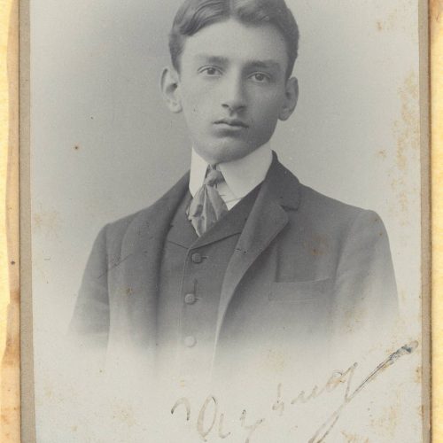 Photographic portrait of a boy in a suit and necktie, bearing his handwritten signature ("Alekos"). The portrait is undated, 
