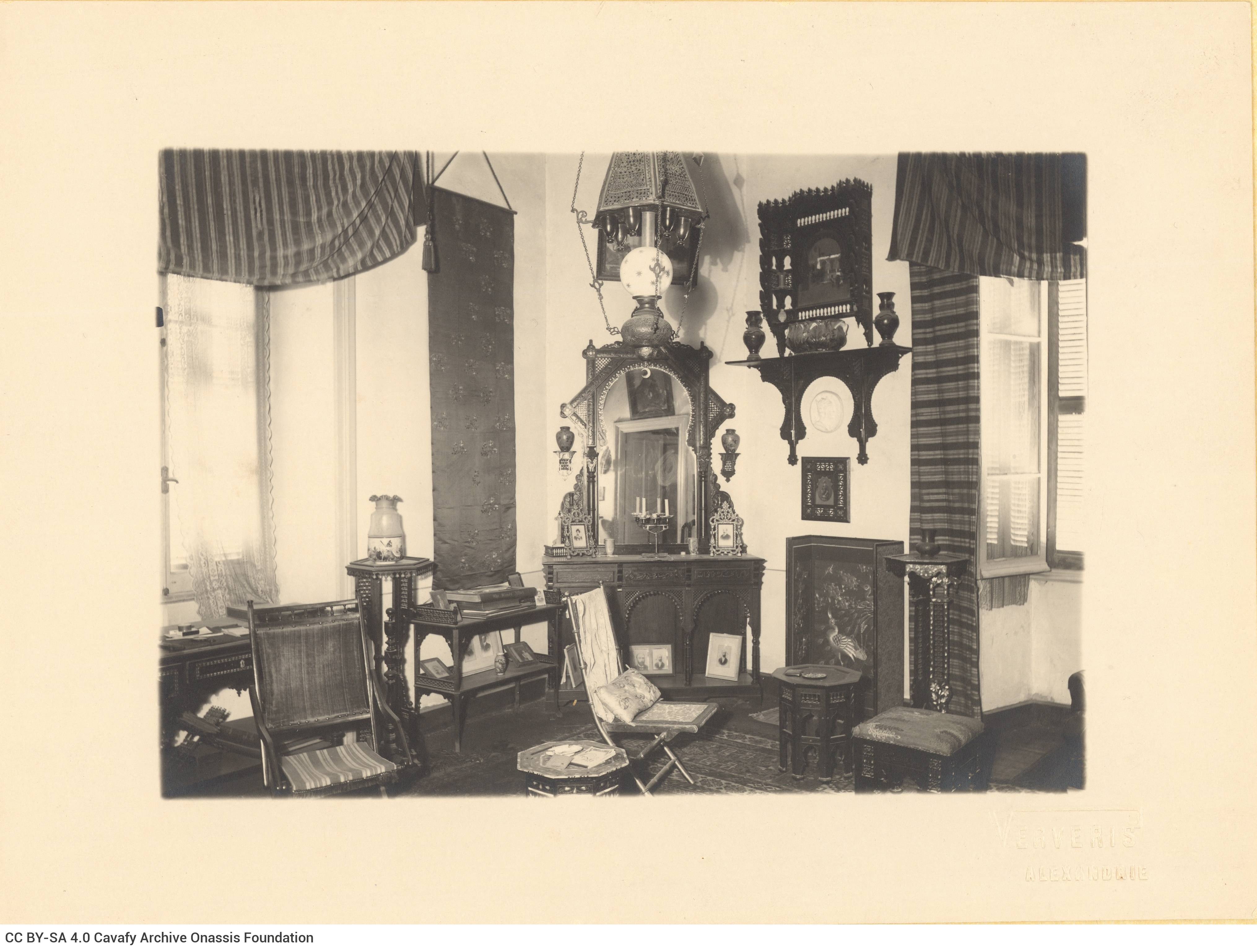 View of the interior of Cavafy's flat. It depicts the living room, with chairs, a desk and a console table with a mirror. The