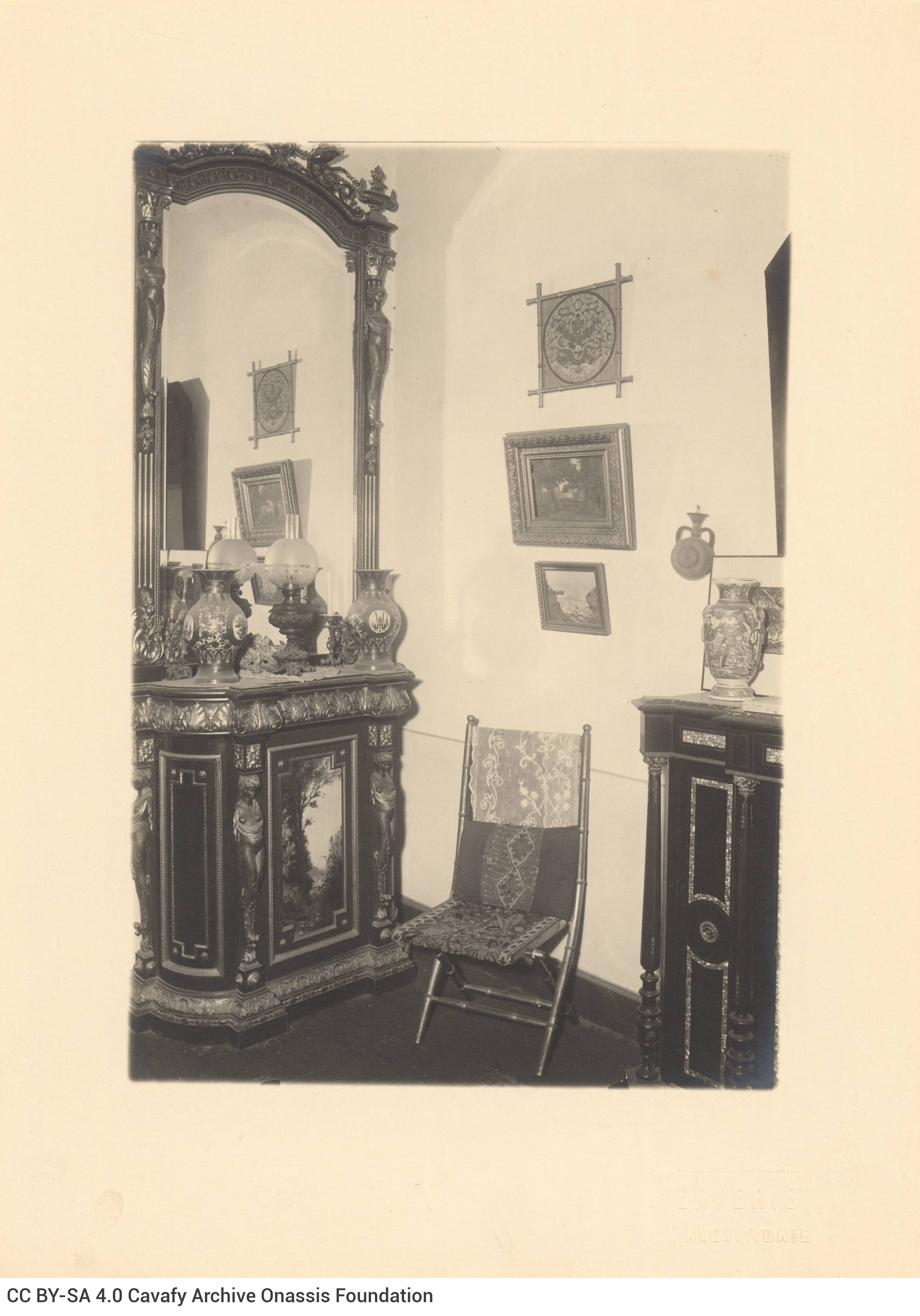 Photograph of the interior of Cavafy's flat. View of the living room, with a console table and a mirror, a seat and frames on
