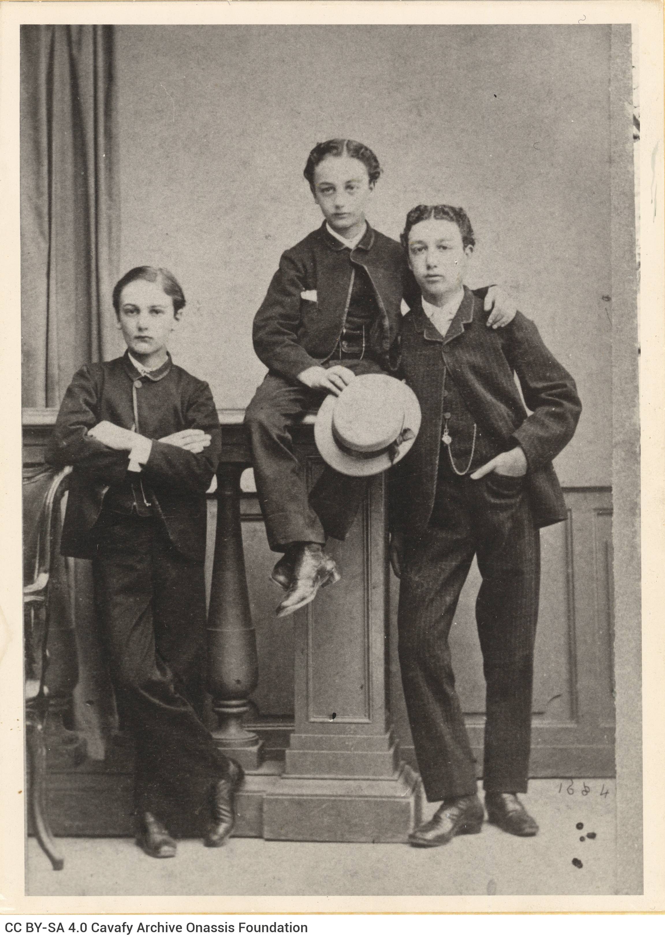 Photograph of three boys in costumes. The boy in the middle stands on a piece of furniture and holds a hat in his right hand.